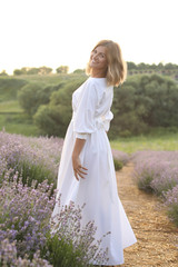 Fototapeta na wymiar smiling attractive woman in white dress posing in violet lavender field