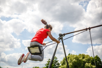 A little girl has fun while swinging in a park, on a summer day