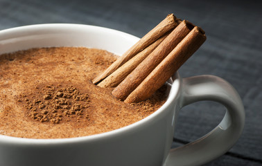 Close up white cup of salep milky hot drink of Turkey with cinnamon powder healthy spice on black wooden background - obrazy, fototapety, plakaty