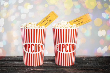 Paper cups of tasty popcorn with cinema tickets and blurred lights on background