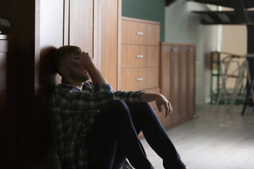 Depressed young man sitting on floor in kitchen