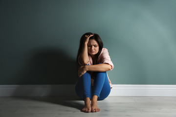 Depressed young woman on floor near color wall