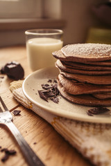 A view of delicious cocoa pancakes with dark chocolate and powdered sugar on a wooden table