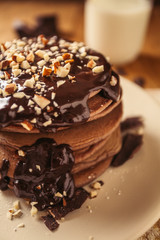 A view of delicious cocoa pancakes with dark chocolate and powdered sugar on a wooden table