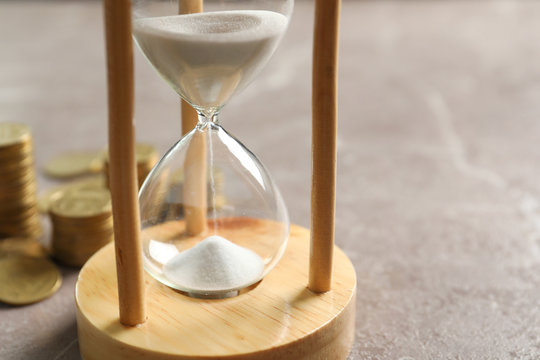 Hourglass with flowing sand and coins on table. Time management