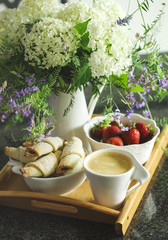Coffee, rugelach with chocolate filling, strawberries and flowers on wooden tray.