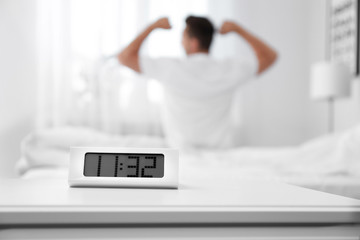 Digital alarm clock and blurred man on background. Time of day