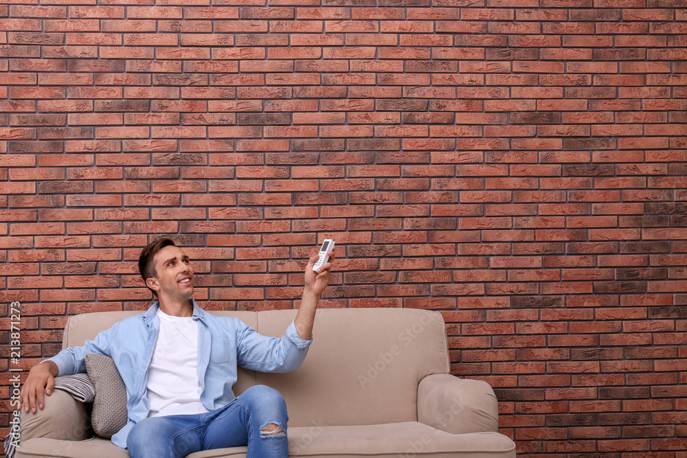 Canvas Prints young man operating air conditioner with remote control near brick wall at home