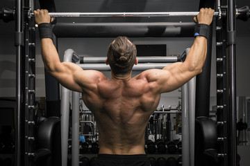 Fototapeta na wymiar Hombre fuerte con grandes músculos haciendo dominadas en el gimnasio de espaldas. Ponerse en forma.