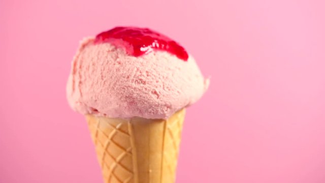 Ice cream. Strawberry or raspberry flavor icecream in waffle cone rotated over pink background. Sweet dessert with strawberry jam topping closeup. 4K UHD video footage. 3840X2160