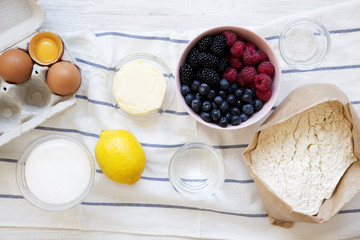 Raw ingredients: berries, flour, eggs, butter, lemon, water, sugar, salt for cooking berry pie on white wooden background, top view. Flat lay. Closeup.