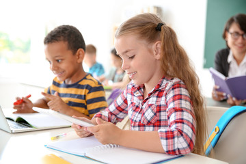 Fototapeta premium Cute little children with gadgets sitting at desk in classroom. Elementary school