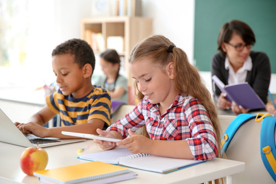 Cute little children with gadgets sitting at desk in classroom. Elementary school