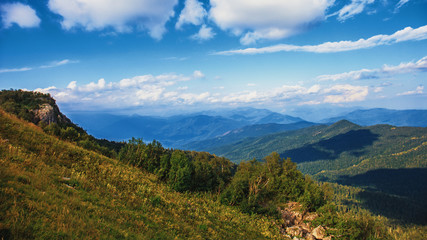 Majestic mountains landscape panorama. Bright blue sky with fluffy clouds and ranges of mountains in myst
