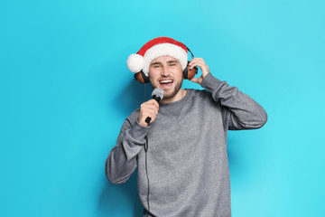 Young man in Santa hat singing into microphone on color background. Christmas music