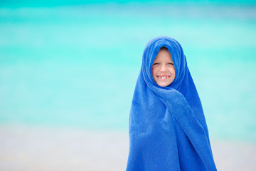 Adorable little girl wrapped in towel at tropical beach after swimming in the sea