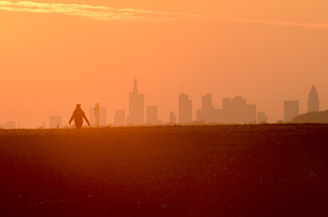 Eine Person geht im Sonnenuntergang vor der Skyline von Frankfurt am Main auf der Hohen Straße spazieren