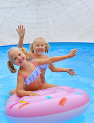 Twin sisters dressed in the same swim suits  sit on a swim ring and enjoy their swimming activities in summer. 