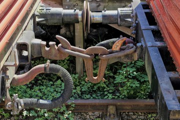 The rusty couplings on old vintage railway trucks or wagons on an overgrown disused railway line or track