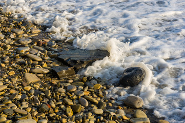 pebble stones on the sea beach, the rolling waves of the sea with foam
