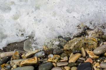 pebble stones on the sea beach, the rolling waves of the sea with foam