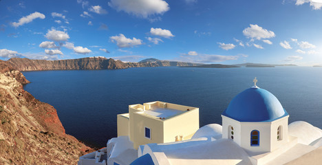 Fototapeta na wymiar Panoramic image of local church with blue cupola in Oia on Santorini island
