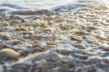 pebble stones on the sea beach, the rolling waves of the sea with foam
