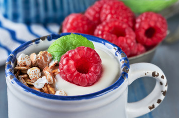 Yogurt with muesli, raspberry and mint leaves, healthy dessert on light blue stripy background