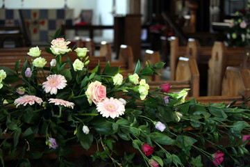 Beautiful display of pink and yellow flowers, behind the rows of wooden pews in a traditional stone built church, with the altar in out of focus background