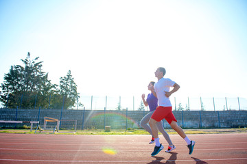 Young sportive couple warming up legs before jogging on running track at sports stadium