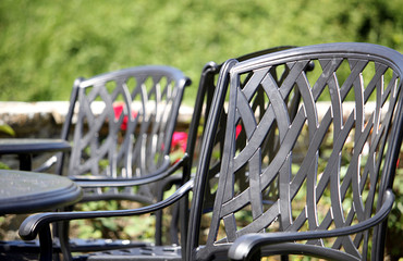 Close up of a wrought iron chair, with other similar chairs and tables in the out of focus background on a lovely sunny day - obrazy, fototapety, plakaty