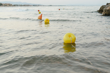Buoys floating near the beach and the rocks of the coast at sunset without bathers.