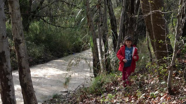 Little girl has a hard time walking on an uneven riverbank in a forest