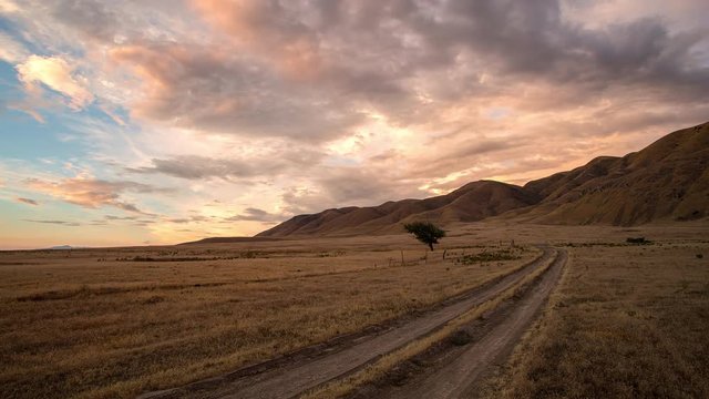 Colorful sunset over dirt road in gold grassy field as the sun sets.