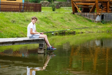 cute boy in white T shirt fishing in the lake and has fun, smiles. vacation with kids, holidays, active weekends concept