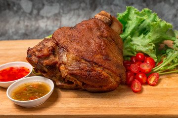 Pork knuckle or German pork hocks with vegetable and fruit served with sauce on chopping board and on wooden table.