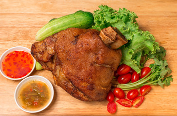 Pork knuckle or German pork hocks with vegetable and fruit served with sauce on chopping board and on wooden table.