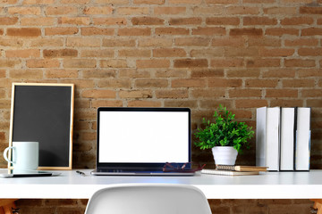 Front view mockup laptop with poster on white table and red brick wall. Blank screen laptop and poster frame for graphic display montage.