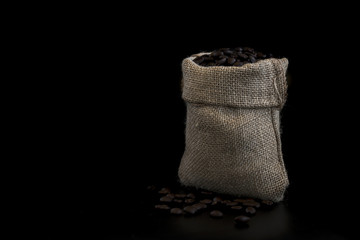 A small sack bag full of fresh coffee beans on a black background.