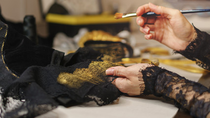 Girl is a fashion designer sewing an evening dress. Shooting close-up. She is gilding the lace. Woman holding paint brush with paint in hands