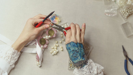 Girl makes fashion jewelry. Shooting close-up. She fixes the fastenings on the decoration with pearls and artificial flowers. Crafting items