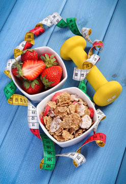 Strawberries, wheat and rye flakes, dumbbells and centimeter, healthy and sporty lifestyle
