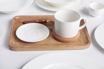 close up view of wooden tray, various plates and bowl with cup on white table
