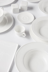 high angle view of different plates, cups, saltcellar and pepper caster on white table