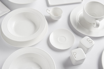 high angle view of different plates, cup, bowl, saltcellar and pepper caster on white table