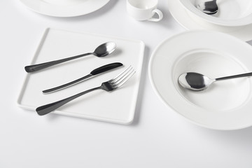 close up view of various plates, cup, fork, knife and spoons on white table