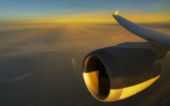 Through window view of plane engine and wing against rising sunrays