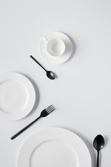 top view of plates, cup, fork and black spoons on white table