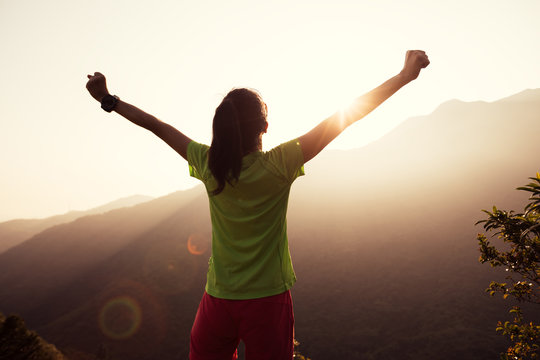 successful woman raised arms to summer sunrise on mountain top