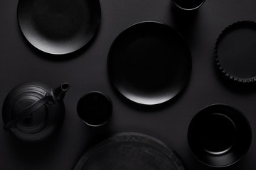 top view of black teapot, plates, bowl, cups, tray and baking dish on black table